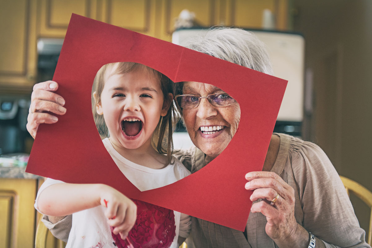 Grandmother and grandchild holding a cutout heart to their faces for a picture