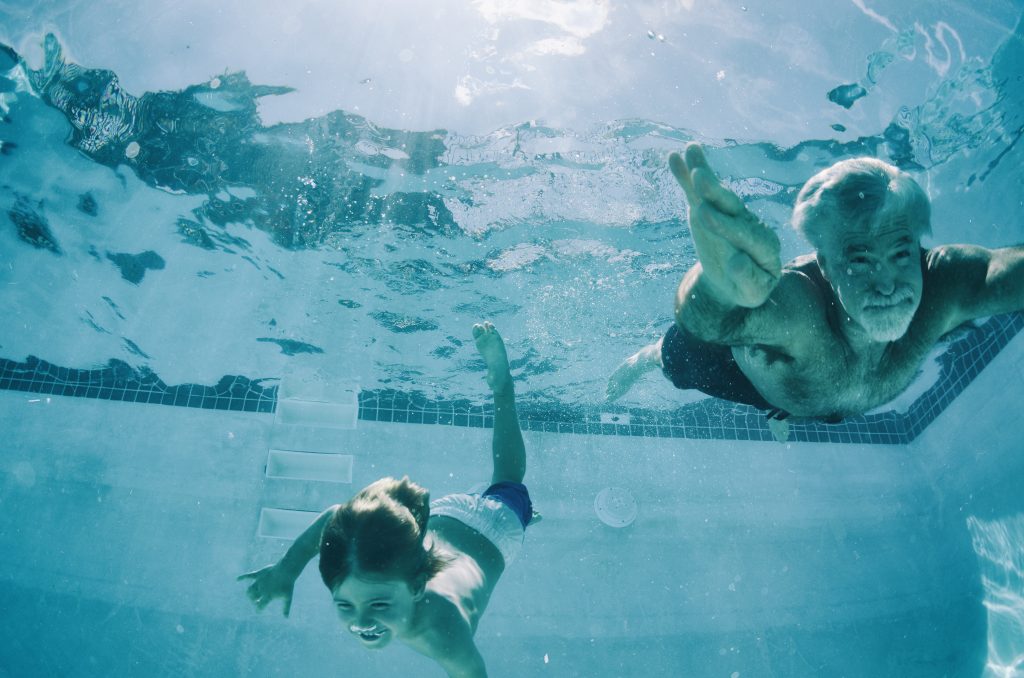 Grandpa and Grandson swimming underwater in pool in summer